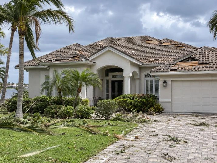 A Southwest Florida home after a storm, with missing roof tiles and palm debris on the lawn and driveway.