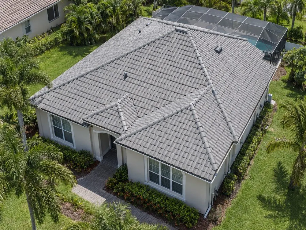 An aerial view of a single-storey Florida home’s grey tile roof among palm trees.