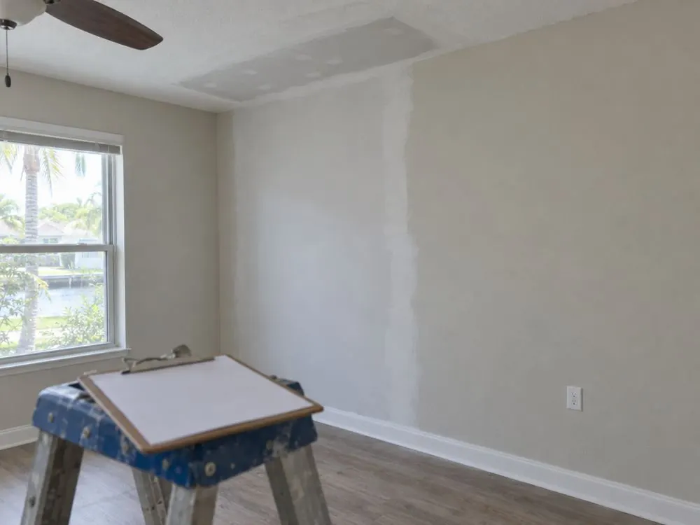 A room with newly patched and primed drywall on the wall and ceiling after water damage repairs.